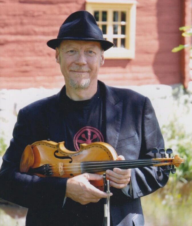 Magnus Gustafsson står utomhus med en fiol i händerna.